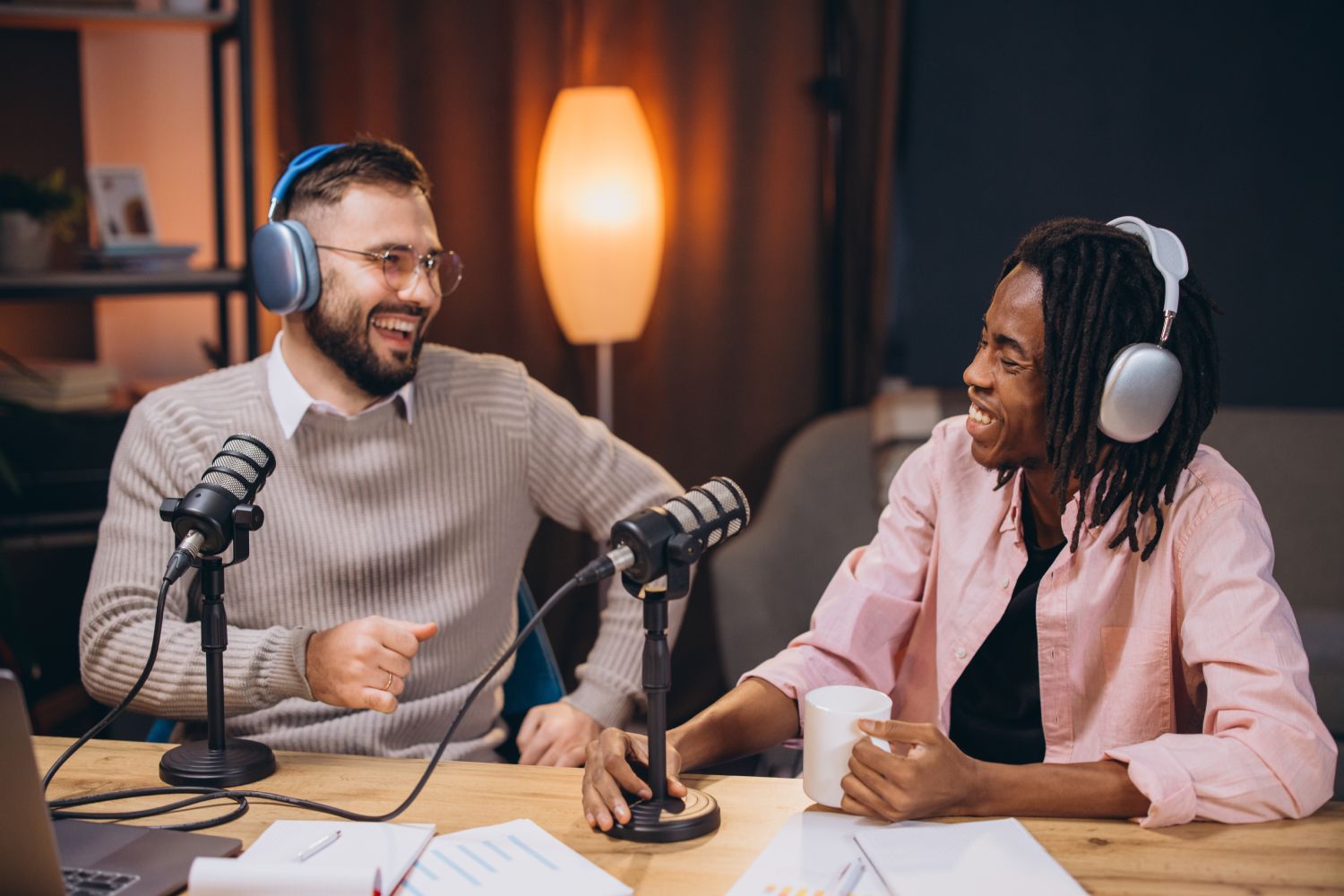 Two male podcasters wearing headphones and laughing while recording a new podcast episode in their studio